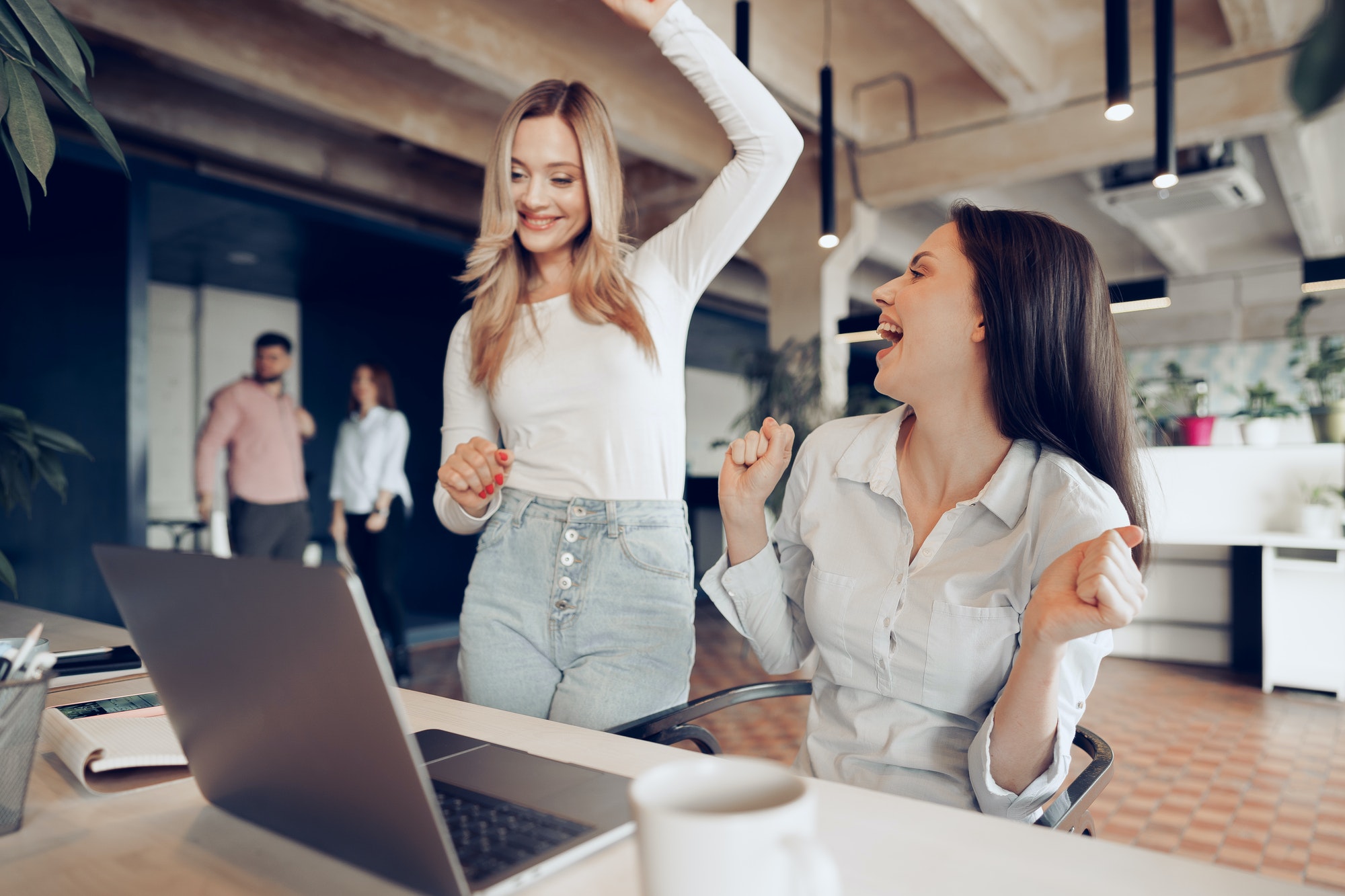Two young happy businesswomen celebrating project success in office